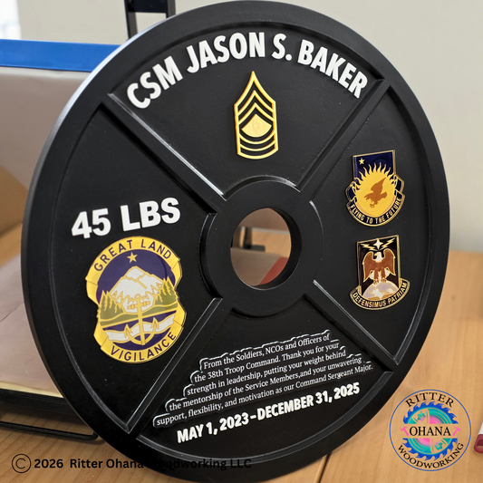 Black round weight plate with engraved text and military unit logos on a wooden surface