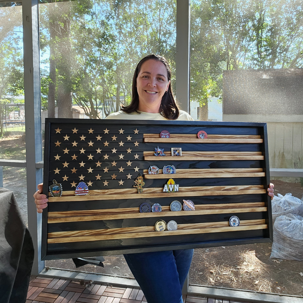 Person holding a wooden American flag with tracks in the stripes to hold challenge coins